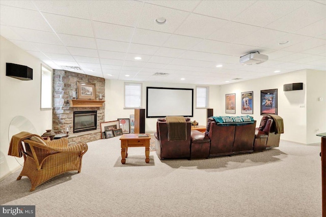 carpeted home theater room featuring a stone fireplace, a healthy amount of sunlight, and a paneled ceiling