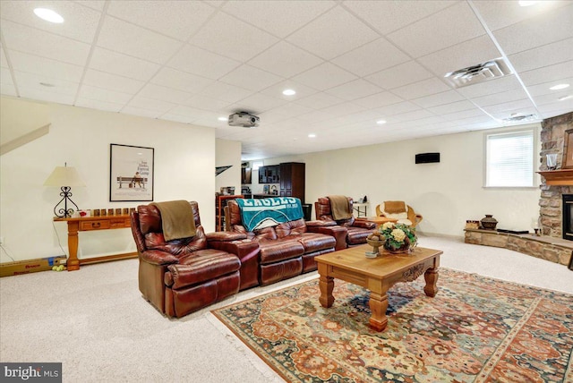 living room featuring a paneled ceiling, a stone fireplace, and carpet floors