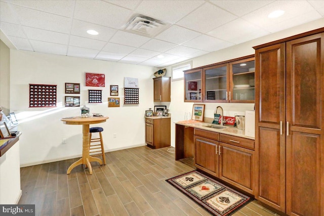 kitchen with a kitchen breakfast bar, sink, a paneled ceiling, and light hardwood / wood-style floors