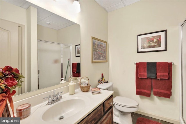 bathroom featuring a paneled ceiling, vanity, toilet, and a shower with door