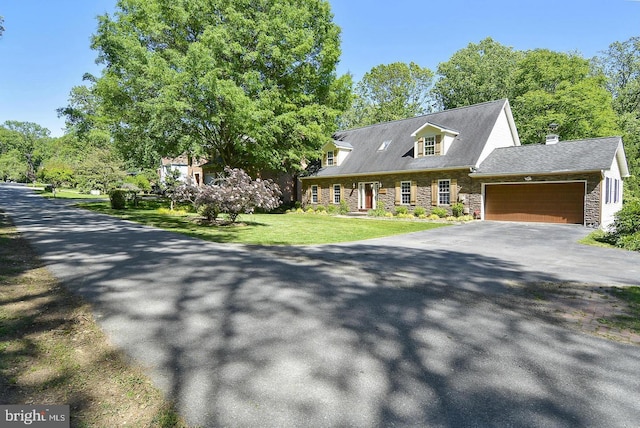 new england style home with a garage, stone siding, driveway, and a front lawn