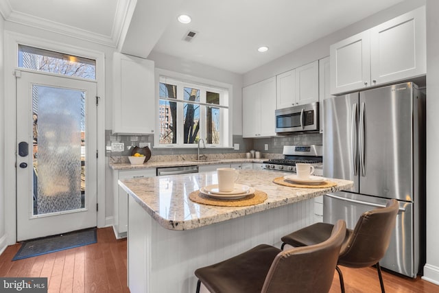 kitchen with a breakfast bar area, white cabinetry, a center island, stainless steel appliances, and light stone countertops