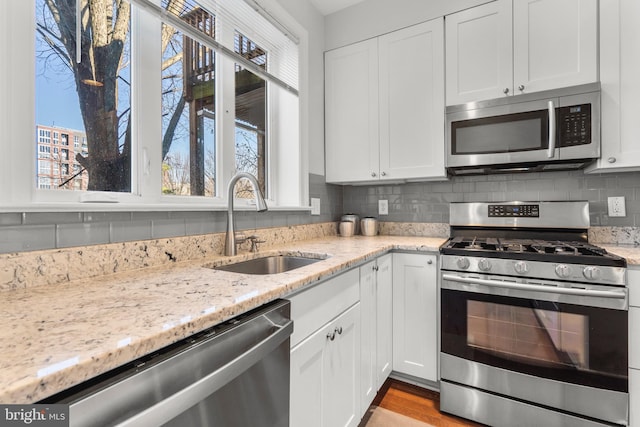 kitchen with stainless steel appliances, white cabinetry, light stone countertops, and sink