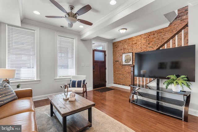 living room with crown molding, wood-type flooring, ceiling fan, and brick wall