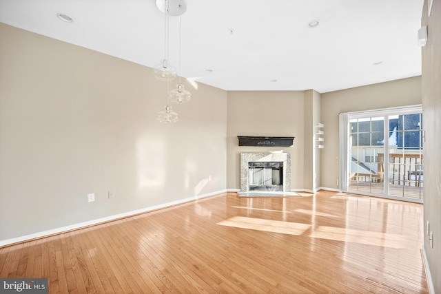 unfurnished living room with a premium fireplace, a chandelier, and light wood-type flooring