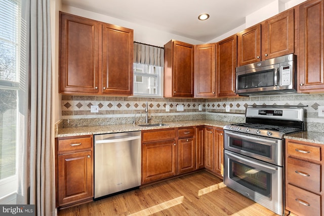 kitchen with sink, light stone counters, appliances with stainless steel finishes, light hardwood / wood-style floors, and backsplash