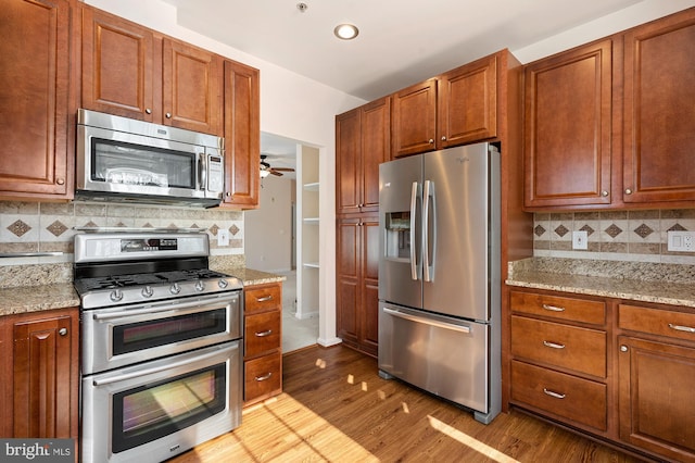 kitchen with ceiling fan, stainless steel appliances, light stone countertops, decorative backsplash, and light wood-type flooring