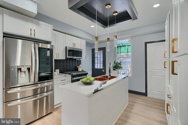 kitchen featuring appliances with stainless steel finishes, decorative light fixtures, white cabinetry, a raised ceiling, and a center island with sink