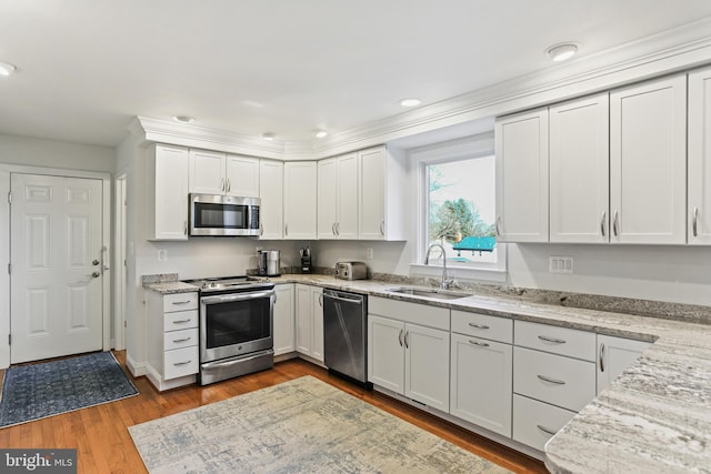 kitchen featuring appliances with stainless steel finishes, sink, white cabinets, light stone countertops, and light hardwood / wood-style flooring