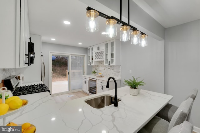 kitchen with sink, appliances with stainless steel finishes, wine cooler, white cabinets, and decorative light fixtures