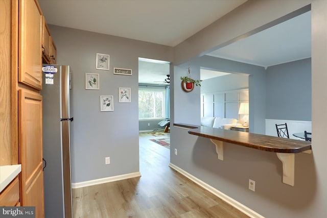 kitchen featuring ceiling fan, a breakfast bar, stainless steel fridge, and light wood-type flooring