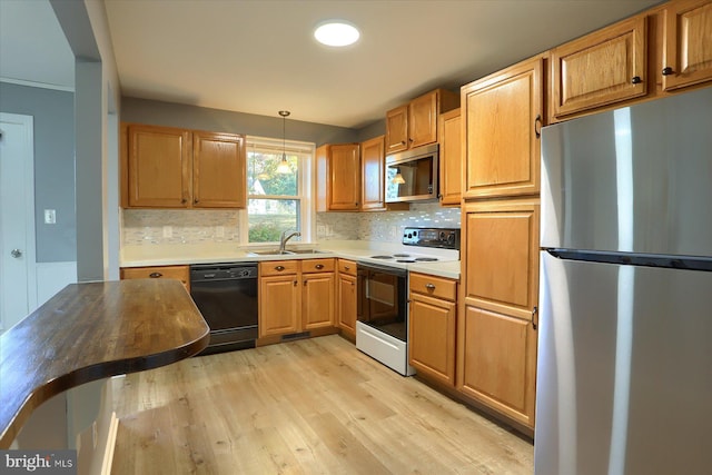 kitchen featuring appliances with stainless steel finishes, pendant lighting, sink, decorative backsplash, and light wood-type flooring