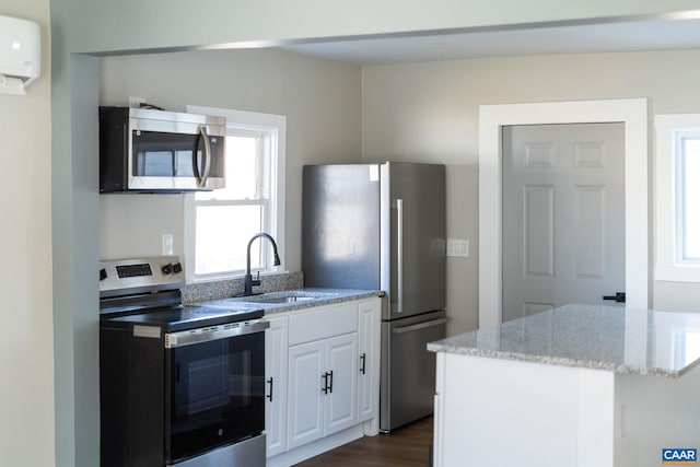 kitchen with sink, an AC wall unit, appliances with stainless steel finishes, light stone countertops, and white cabinets