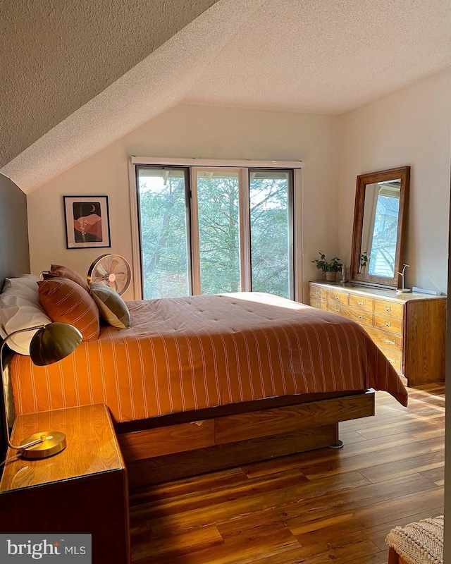 bedroom featuring lofted ceiling, hardwood / wood-style floors, and a textured ceiling