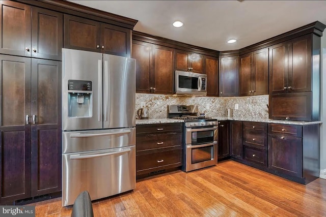 kitchen featuring appliances with stainless steel finishes, backsplash, light stone counters, dark brown cabinets, and light hardwood / wood-style flooring