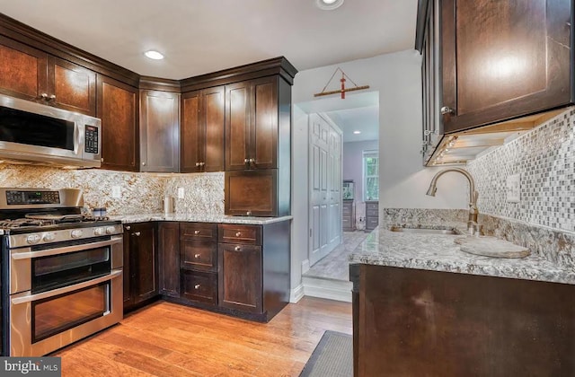 kitchen with appliances with stainless steel finishes, sink, decorative backsplash, light stone countertops, and light wood-type flooring