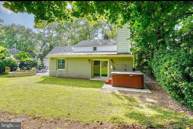 back of property with a hot tub, a patio area, and a lawn