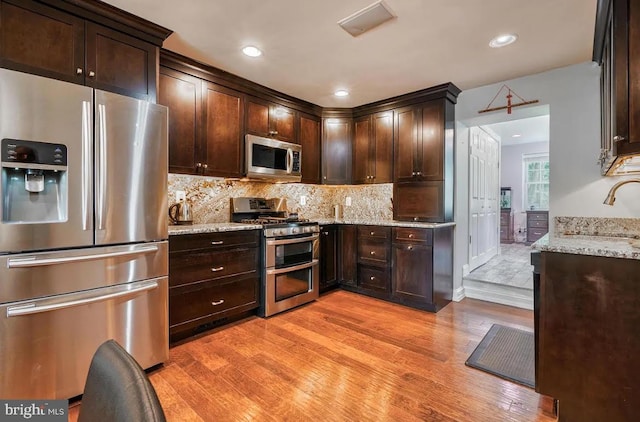 kitchen with appliances with stainless steel finishes, sink, light stone counters, and light wood-type flooring