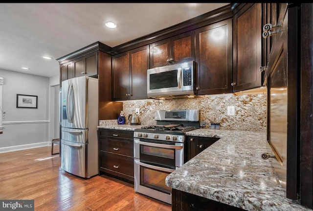 kitchen with stainless steel appliances, dark brown cabinetry, light stone counters, and light hardwood / wood-style floors