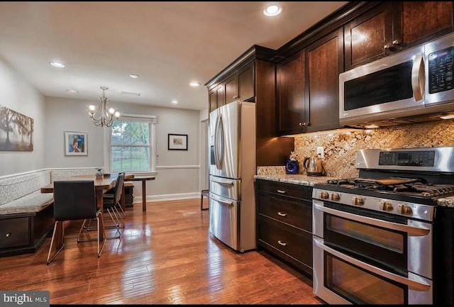 kitchen with dark brown cabinetry, tasteful backsplash, appliances with stainless steel finishes, pendant lighting, and light stone countertops