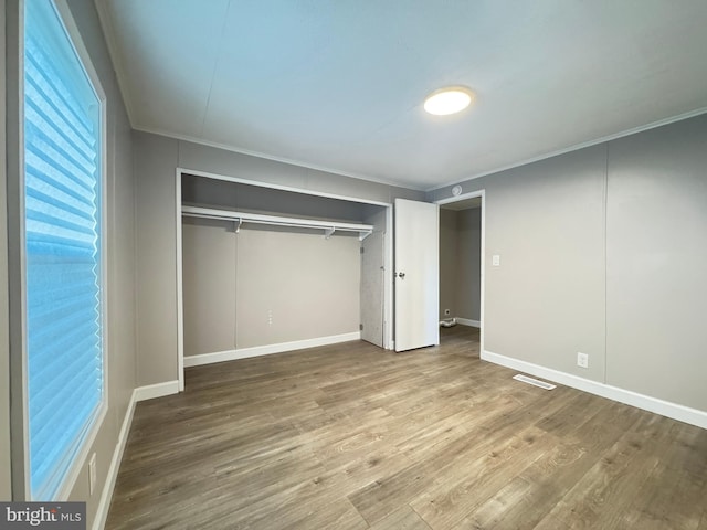 unfurnished bedroom featuring hardwood / wood-style flooring, ornamental molding, and a closet