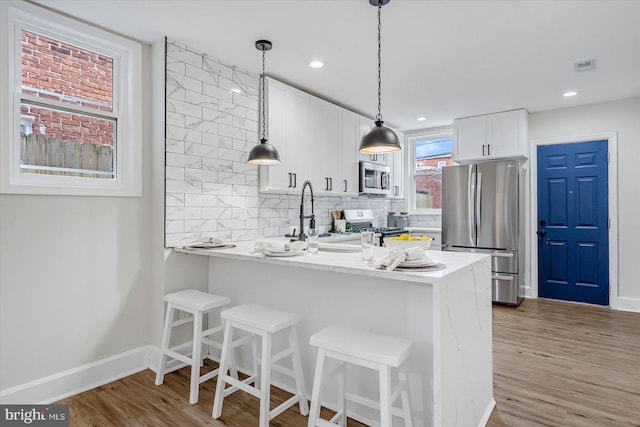 kitchen with white cabinetry, stainless steel appliances, light stone counters, tasteful backsplash, and kitchen peninsula