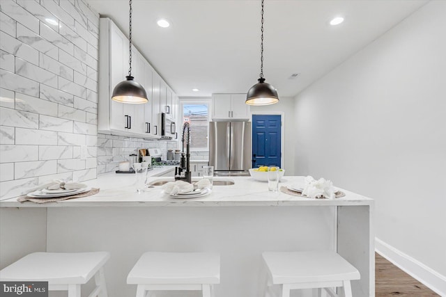 kitchen featuring white cabinetry, a kitchen breakfast bar, stainless steel appliances, light stone counters, and kitchen peninsula