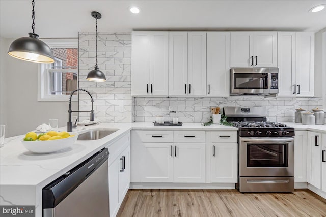 kitchen featuring decorative light fixtures, sink, white cabinets, stainless steel appliances, and light wood-type flooring