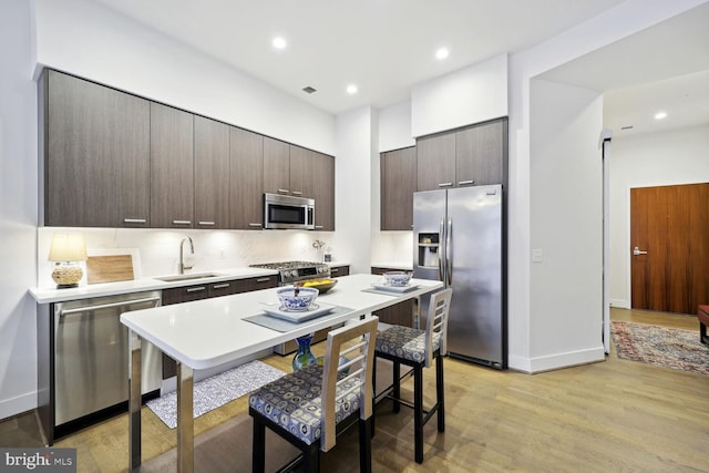 kitchen featuring sink, decorative backsplash, dark brown cabinetry, light hardwood / wood-style floors, and stainless steel appliances