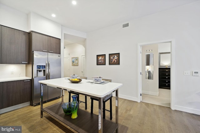 kitchen with dark brown cabinetry, stainless steel fridge, and light hardwood / wood-style flooring