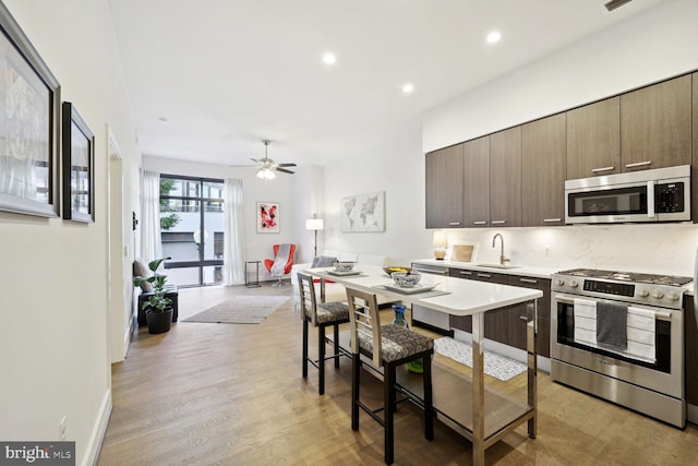 kitchen with sink, light hardwood / wood-style flooring, ceiling fan, stainless steel appliances, and tasteful backsplash