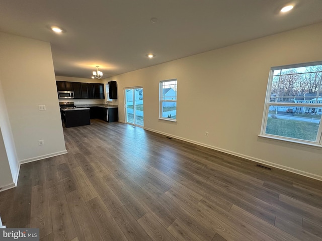 unfurnished living room with an inviting chandelier and dark hardwood / wood-style flooring