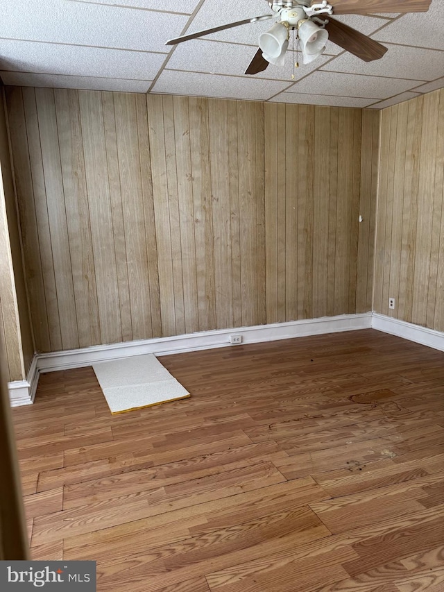 empty room with wood-type flooring, ceiling fan, and wood walls