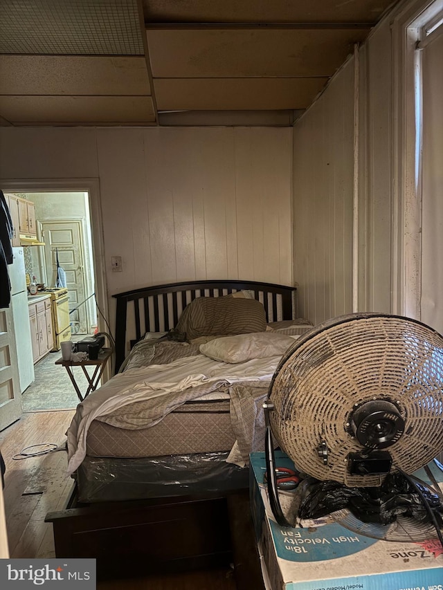 bedroom featuring wood-type flooring, white fridge, and a drop ceiling