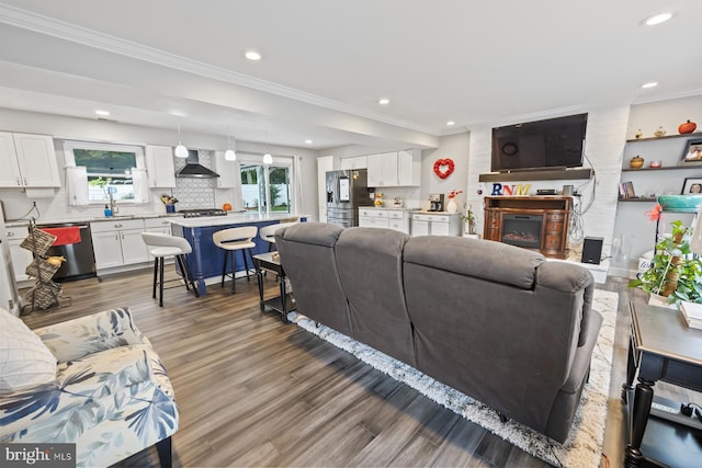 living room with a large fireplace, plenty of natural light, wood-type flooring, and ornamental molding