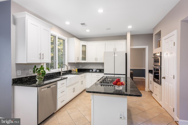 kitchen with stainless steel appliances, white cabinetry, a center island, and dark stone countertops