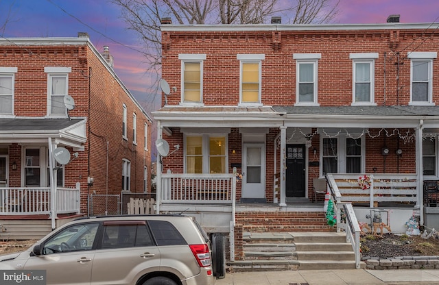 townhome / multi-family property featuring covered porch and brick siding