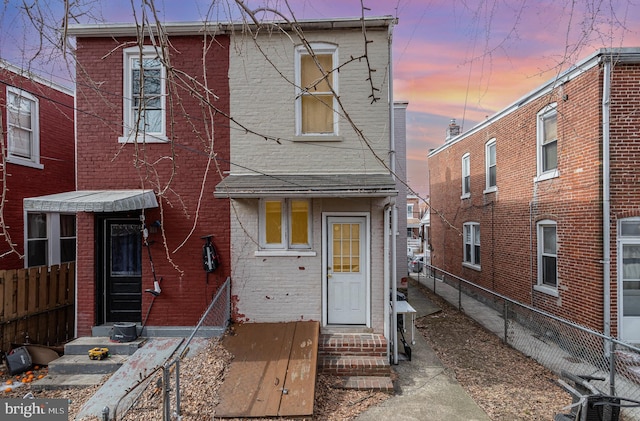 view of front facade with entry steps, brick siding, and fence