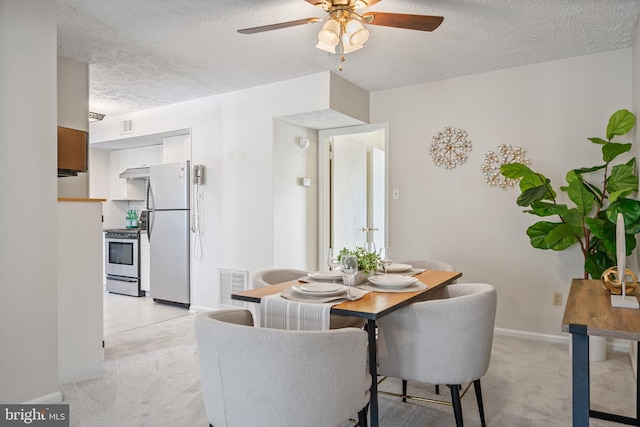 dining area featuring ceiling fan, light colored carpet, and a textured ceiling