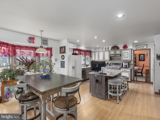 kitchen featuring a kitchen island, under cabinet range hood, stainless steel appliances, light wood-style floors, and backsplash