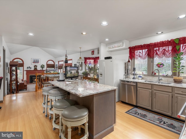 kitchen with light wood finished floors, lofted ceiling, stainless steel dishwasher, a kitchen island, and a sink