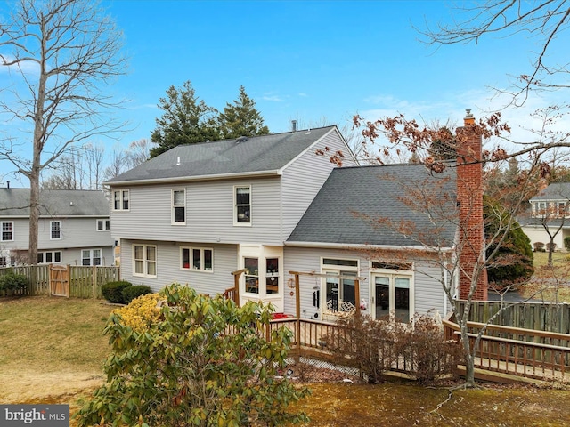 back of property with a deck, fence, a yard, roof with shingles, and a chimney