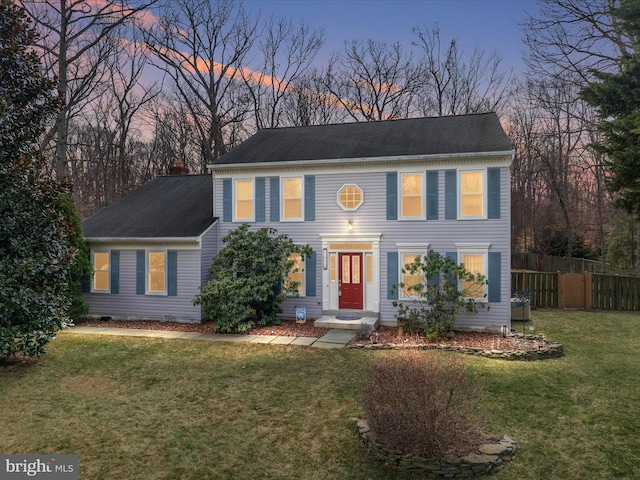 colonial home featuring fence and a lawn