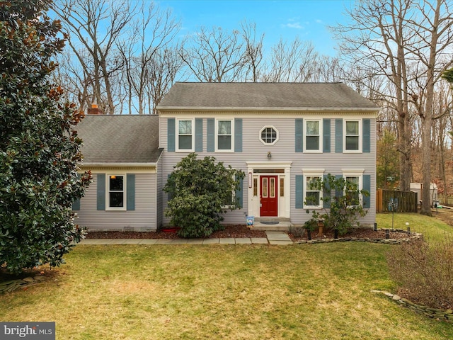 colonial inspired home featuring a shingled roof, a front yard, fence, and a chimney