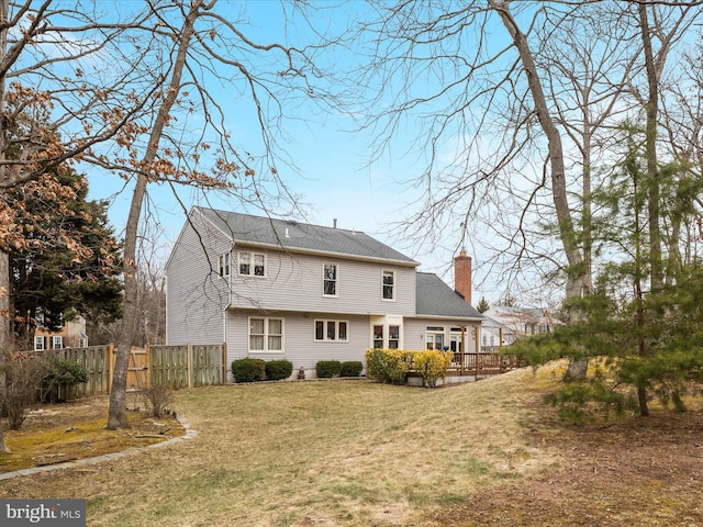 rear view of house featuring a chimney, fence, a deck, and a lawn