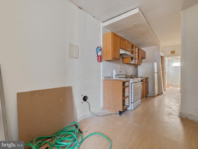 kitchen featuring fridge, white gas stove, light hardwood / wood-style floors, and decorative backsplash