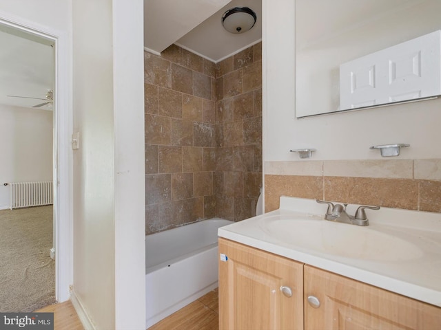 bathroom featuring ceiling fan, tiled shower / bath, radiator heating unit, and vanity