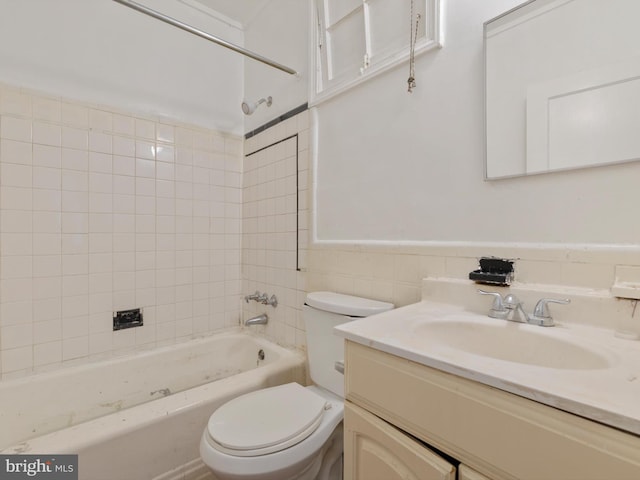 full bathroom with vanity, tiled shower / bath, toilet, and tile walls