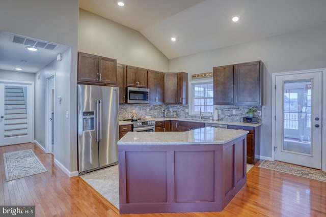 kitchen featuring lofted ceiling, light hardwood / wood-style flooring, stainless steel appliances, light stone counters, and a kitchen island