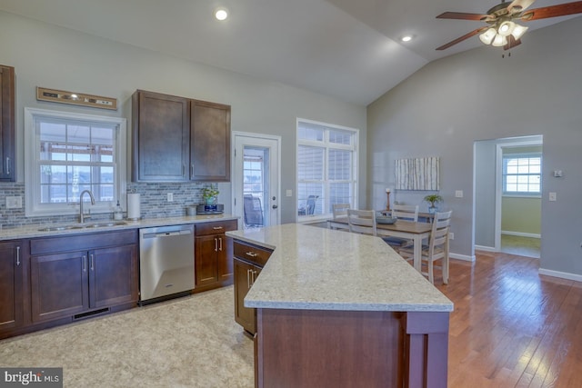 kitchen with sink, vaulted ceiling, dishwasher, a kitchen island, and backsplash